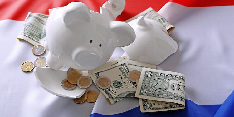 Opengebroken spaarvarken met geld erbij op een vlag van Nederland