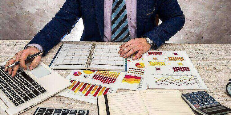Bureaublad met laptop, rekenmachine en papieren met grafieken erop