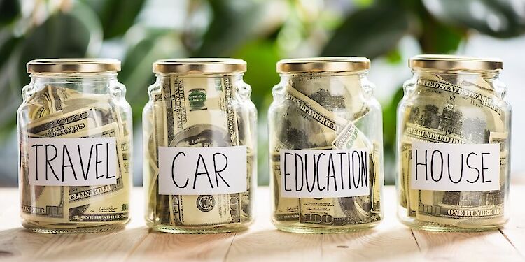 vier potjes met geld erin. Met de woorden 'Travel, 'Car', 'Education' en 'House' erop geplakt