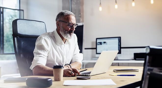 Man achter bureau met laptop en koffie ernaast