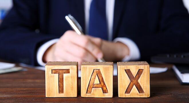 Man aan tafel die iets opschrijft met drie blokjes met tax voor hem