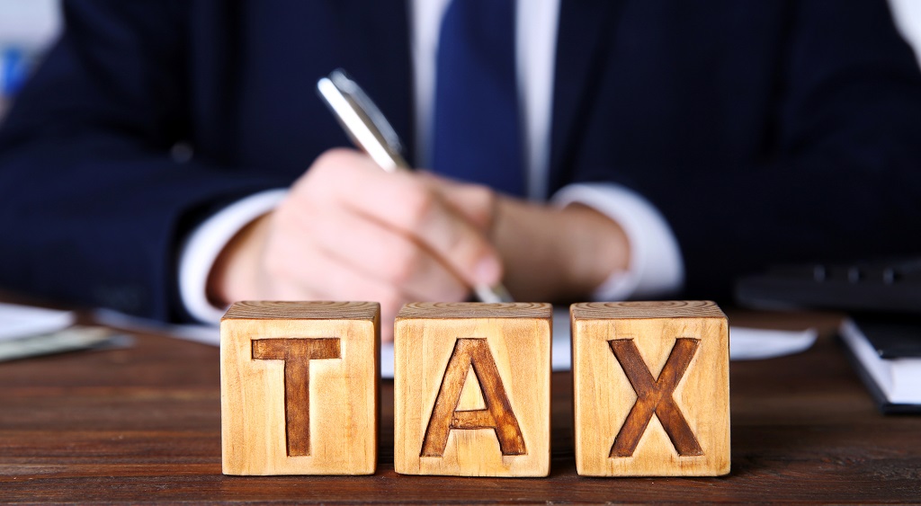 Man aan tafel die iets opschrijft met drie blokjes met tax voor hem
