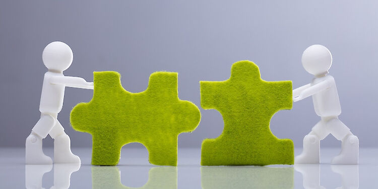 Twee witte poppetjes die groene puzzelstukjes in elkaar duwen