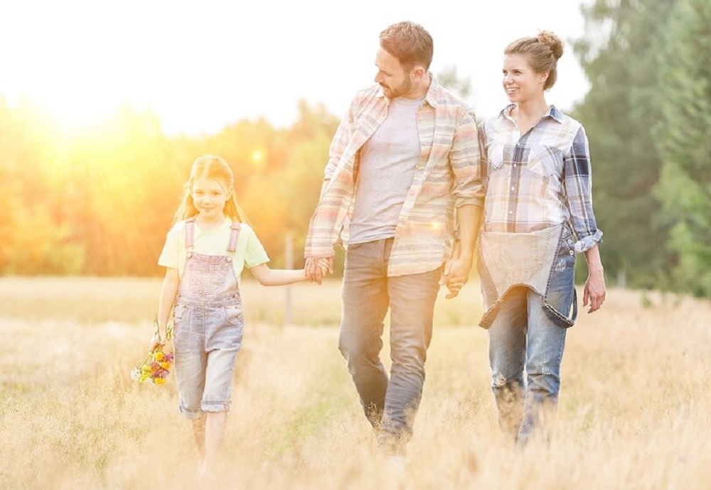 Stel met kind lopen hand en hand door gras met golden hour.