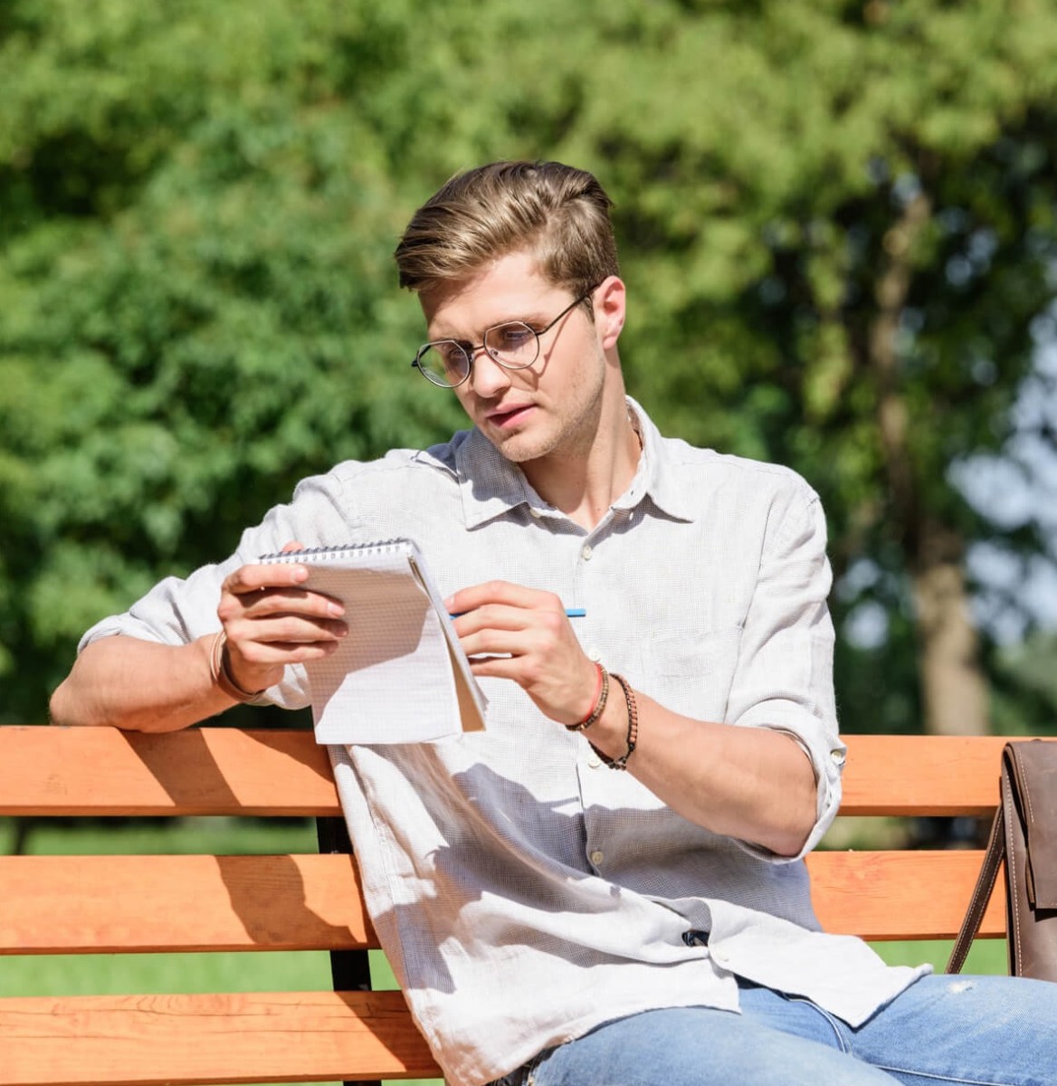 man met notitieboek en pen zittend op bankje in park