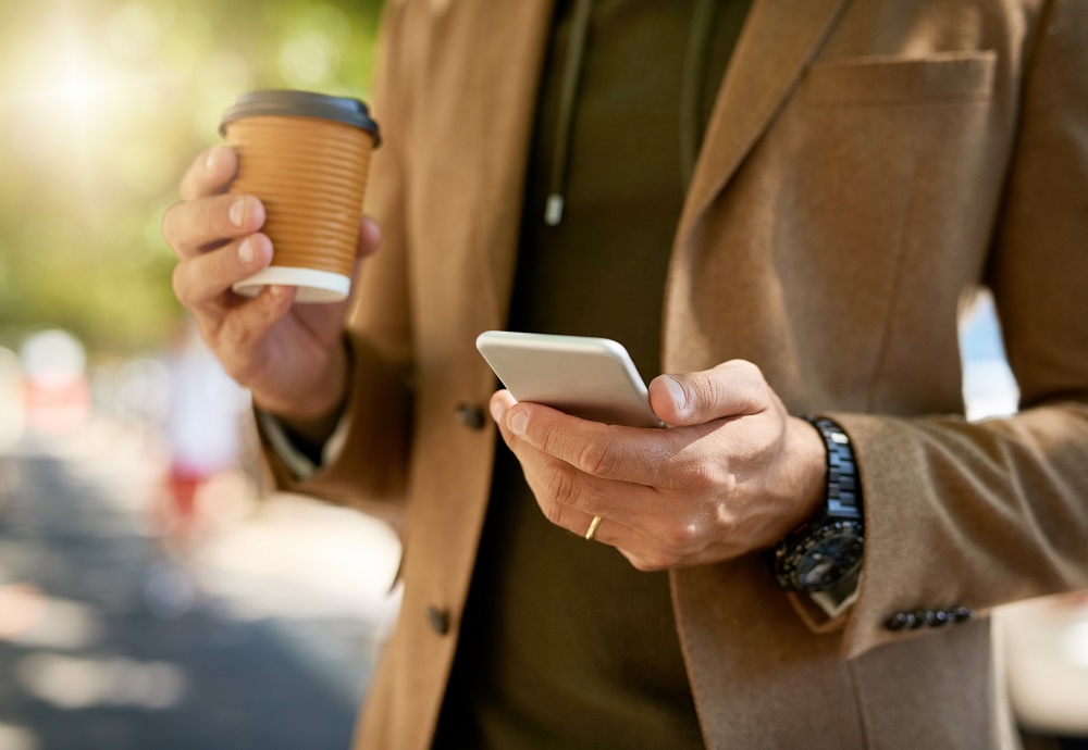 Torso van man met telefoon en koffie in de hand.