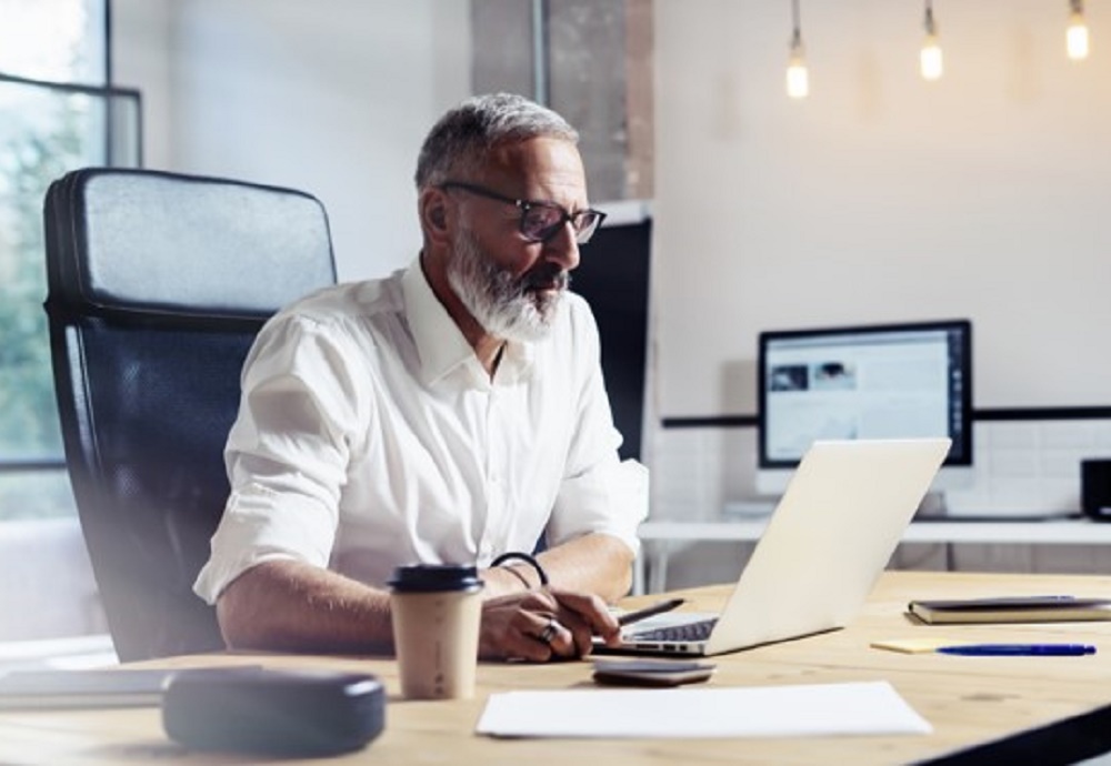 Man in kantoor kijkend naar laptop met een koffie naast hem.