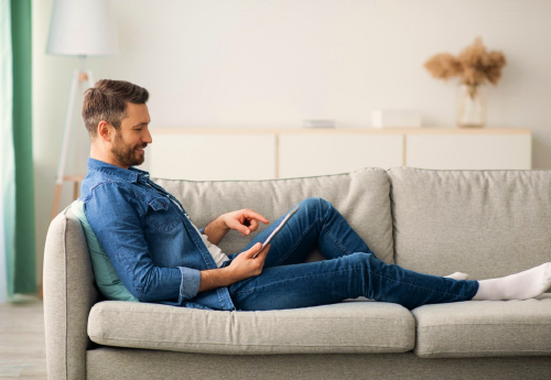 Man zit in bank kijkend naar een tablet in zijn hand en tikt daarop
