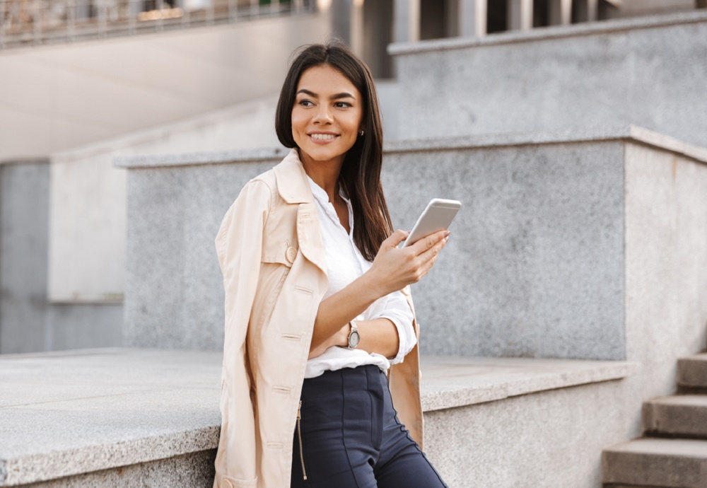 vrouw die tegen een muurtje aan staat met telefoon in hand
